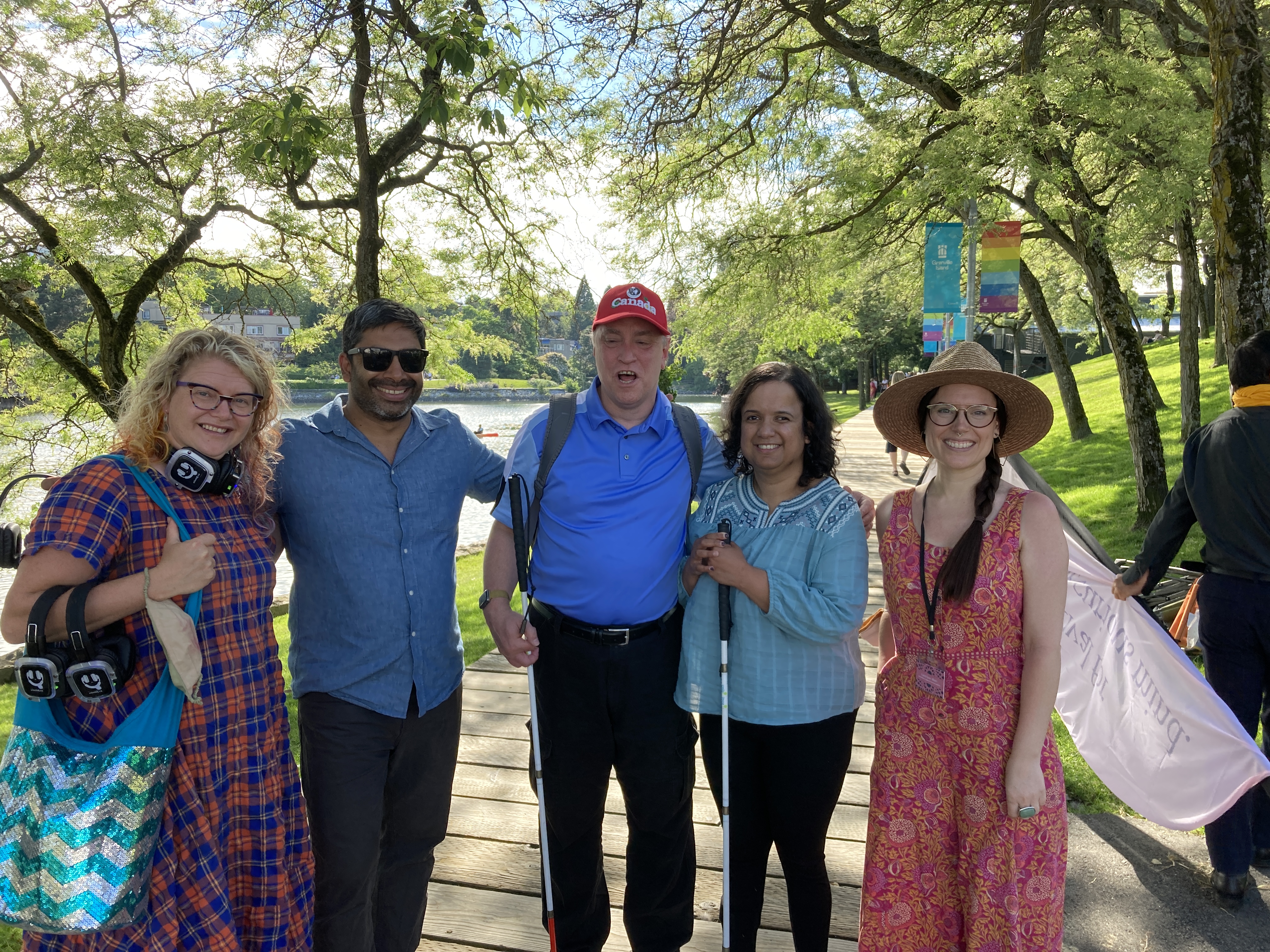 Kristy, Shawn and Annika stand with Indian Summer Festival co-founder Siresh Rao and festival Community Development Director, Laura June with leafy trees and the ocean in the background.